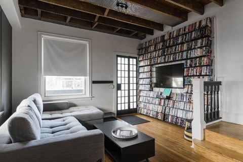 A living room with a grey couch and a wall of DVDs.