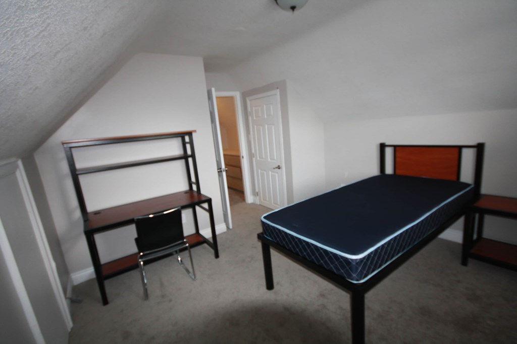 A bedroom with a bed, chair, and shelf.
