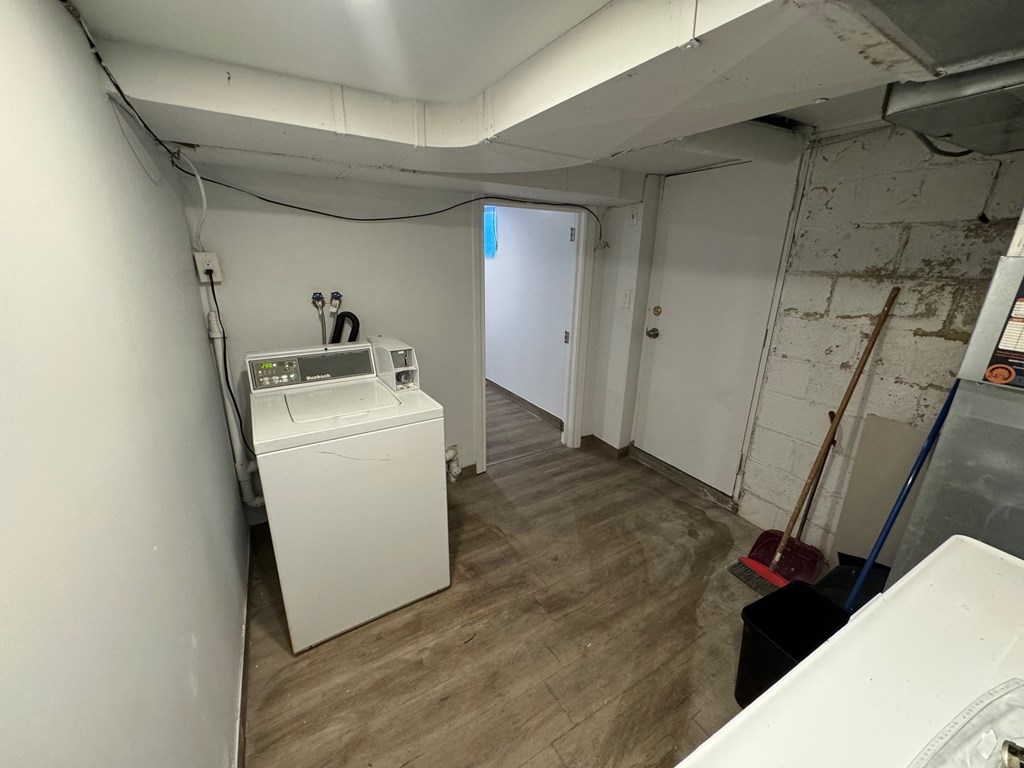 A white washing machine sits in a room with wooden floors and white walls.