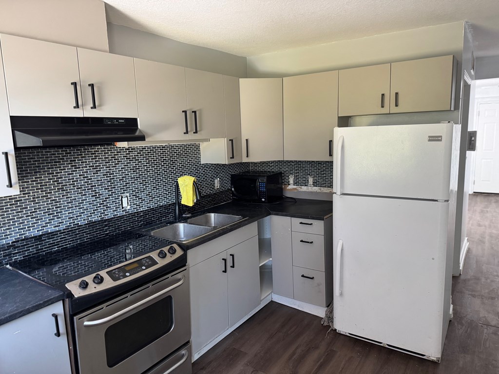 A kitchen with a white fridge and black countertops.