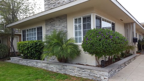 the front of a house with a stone wall and plants