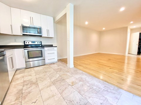 an empty kitchen and living room with white cabinets and stainless steel appliances