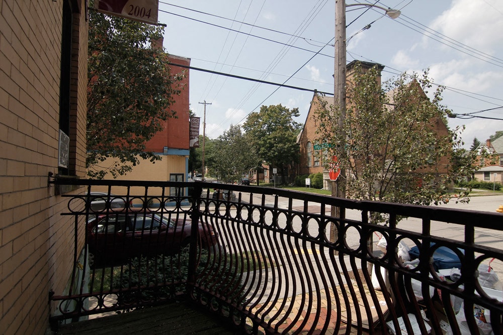 A balcony with a metal railing and a bench overlooks a street.