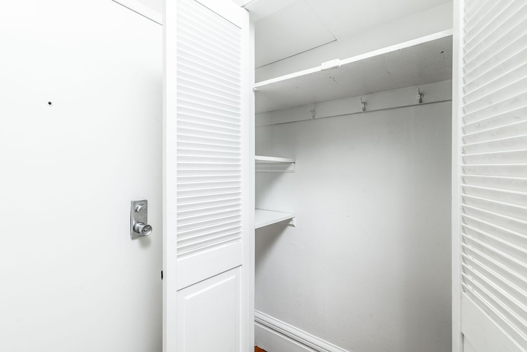 A white door with a silver handle is open to a white interior with a shelf.