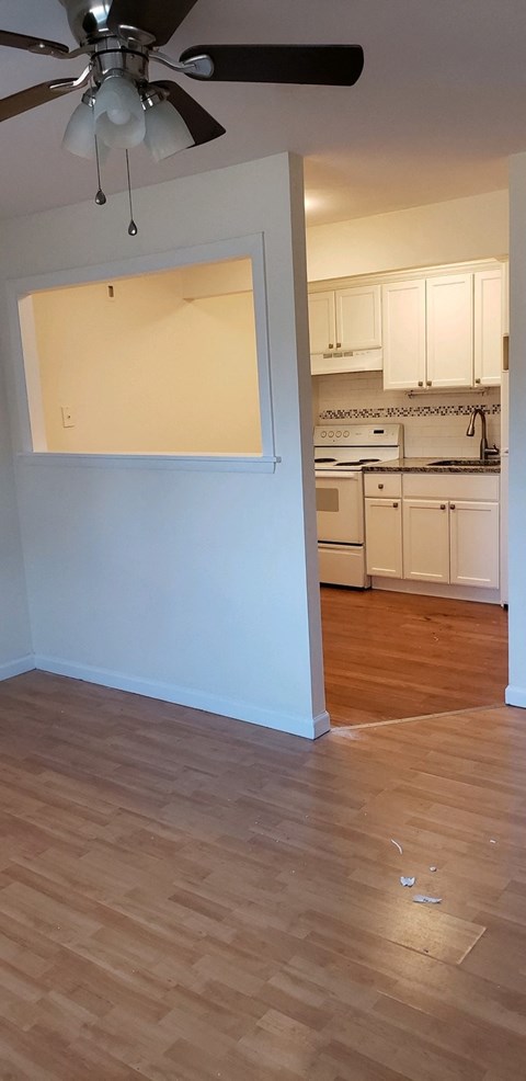 an empty living room and kitchen with wood flooring and a ceiling fan