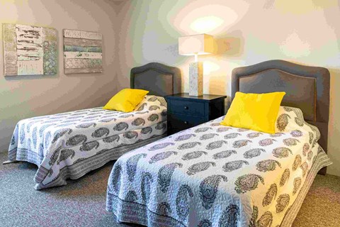 a bedroom with two beds with yellow pillows and a night stand