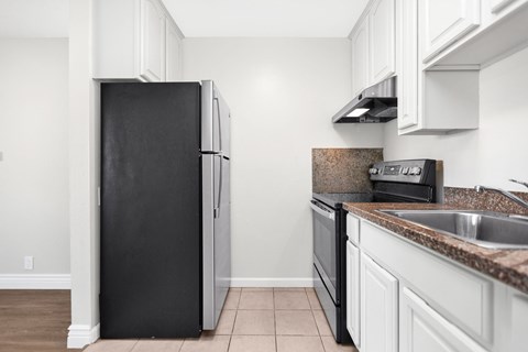 A black refrigerator sits in a kitchen with white cabinets.