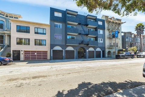 A street view of a multi-story building with a blue facade and a car parked in front.
