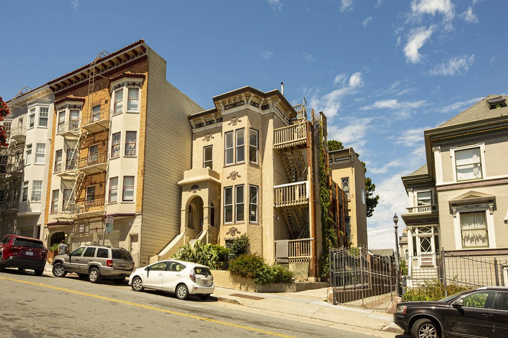 A row of old buildings with cars parked in front.