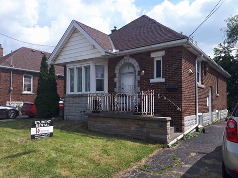 a small brick house with a porch and a street sign in front of it