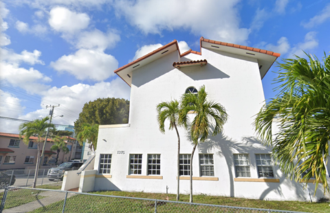 A white house with a red roof and a fence in front.