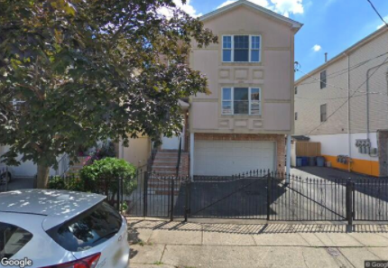A two-story house with a garage is surrounded by a black fence.