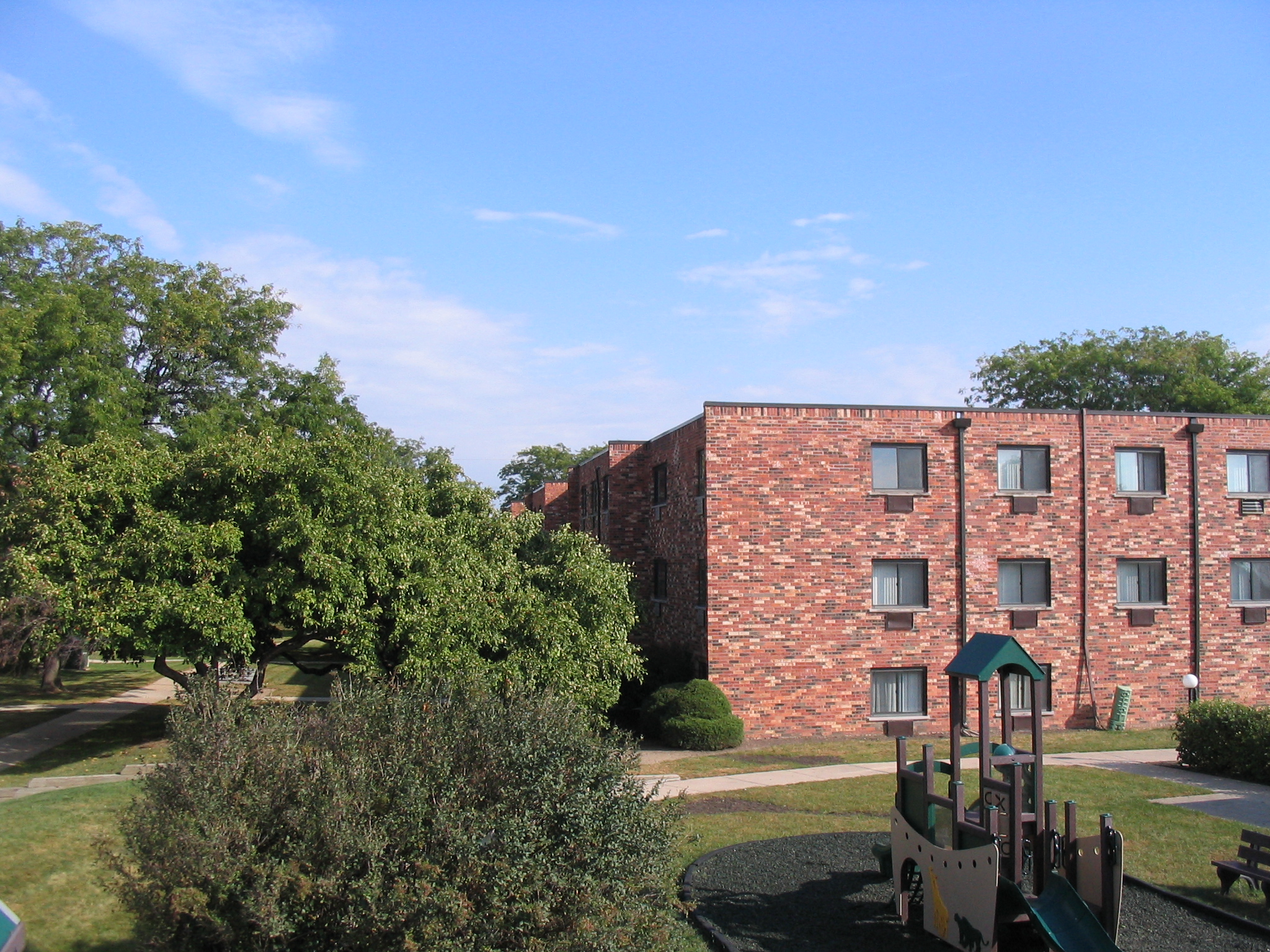 A playground with a slide and a green roof is in front of a red brick building.