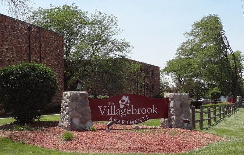 A sign for Villagebrook Apartments is displayed in front of a building.