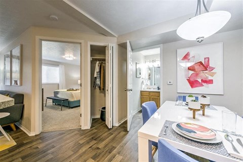 A dining room with a table set for two and a bedroom with a bed in the background.