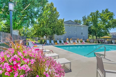 A pool area with a building in the background and a flower bed in the foreground.