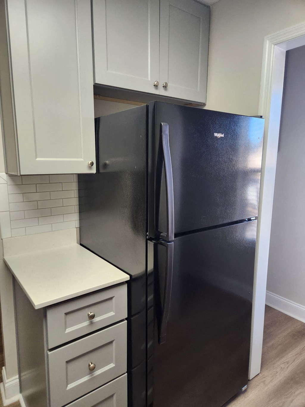 A black fridge in a kitchen with white cabinets.