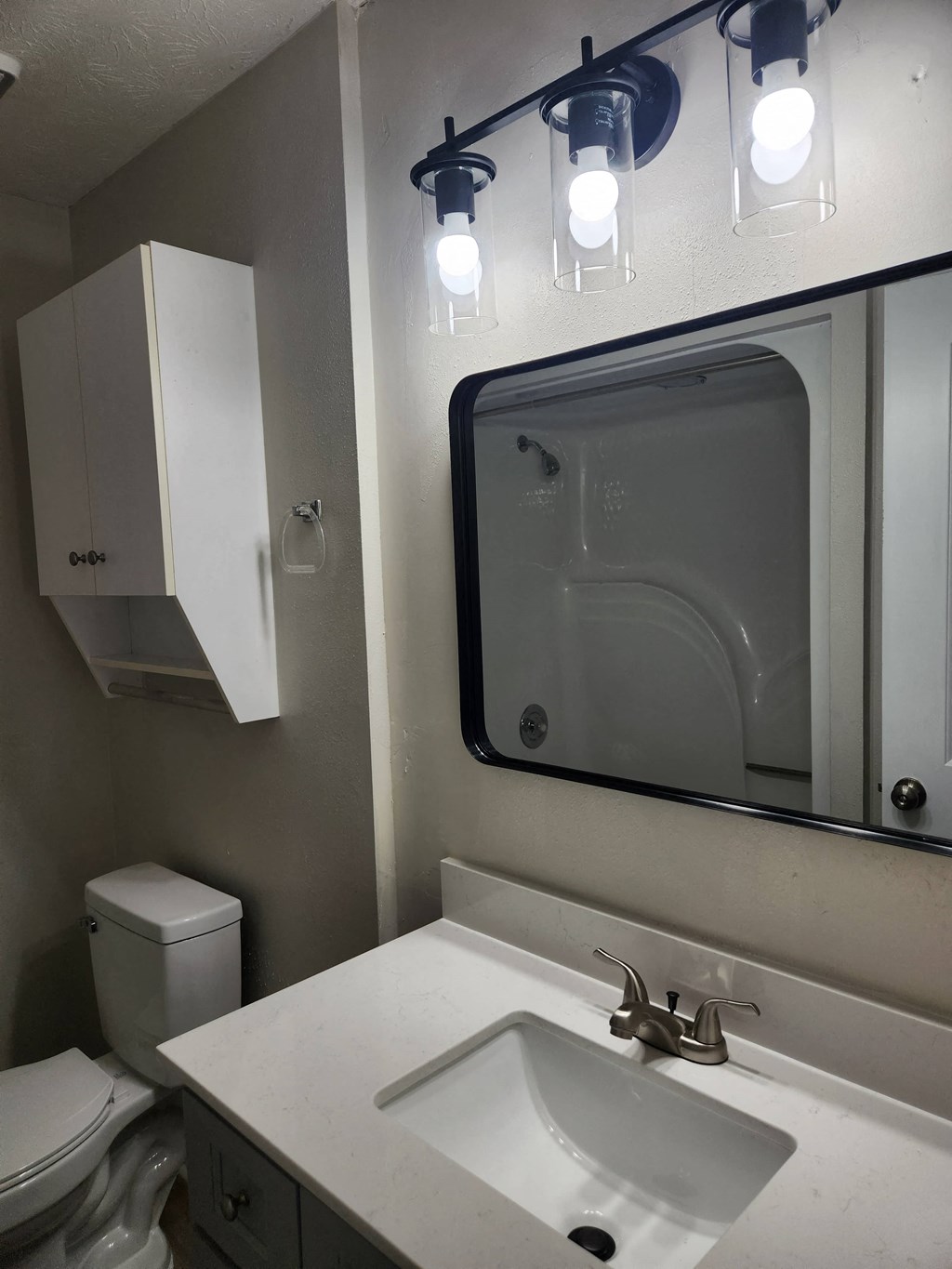 A white bathroom with a toilet, sink, mirror, and light fixture.
