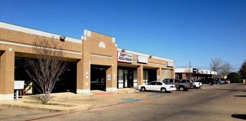 A parking lot in front of a strip mall with a car parked in the lot.