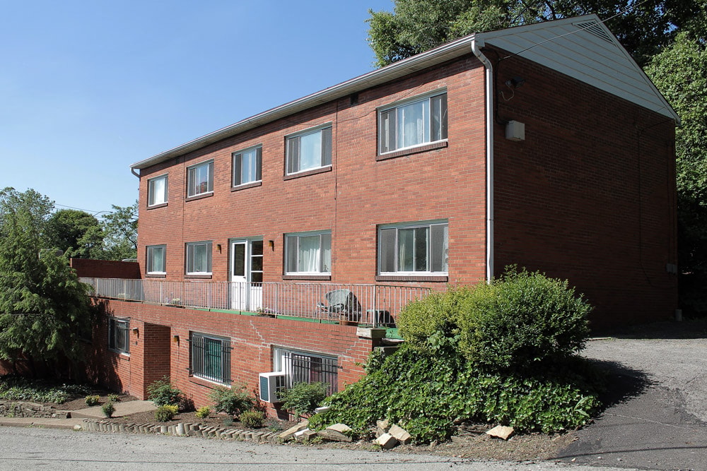 A red brick building with a green bush in front.