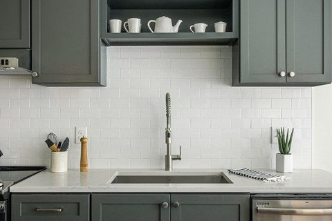 a kitchen with gray cabinets and white tiles and a sink