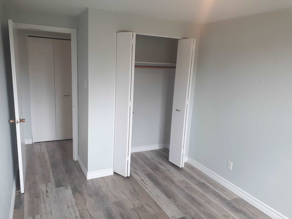 a bedroom with white walls and wood floors and a closet