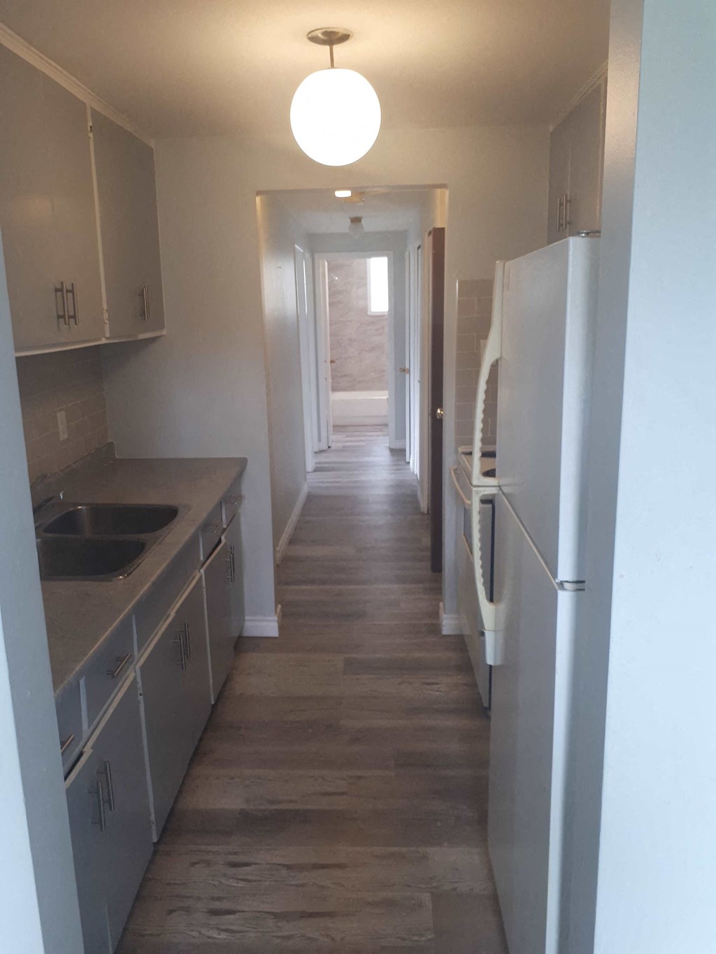a long narrow kitchen with white cabinets and a white refrigerator