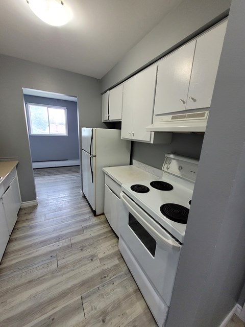 A kitchen with a white stove top oven and white cabinets.