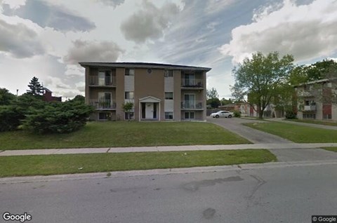 A street view of a residential building with a car parked in front.