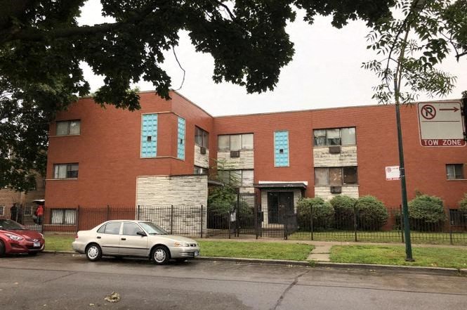 A red car is parked on the street in front of a brick building.
