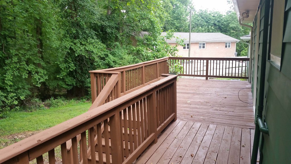 A wooden deck with a railing and a view of a green lawn and trees.