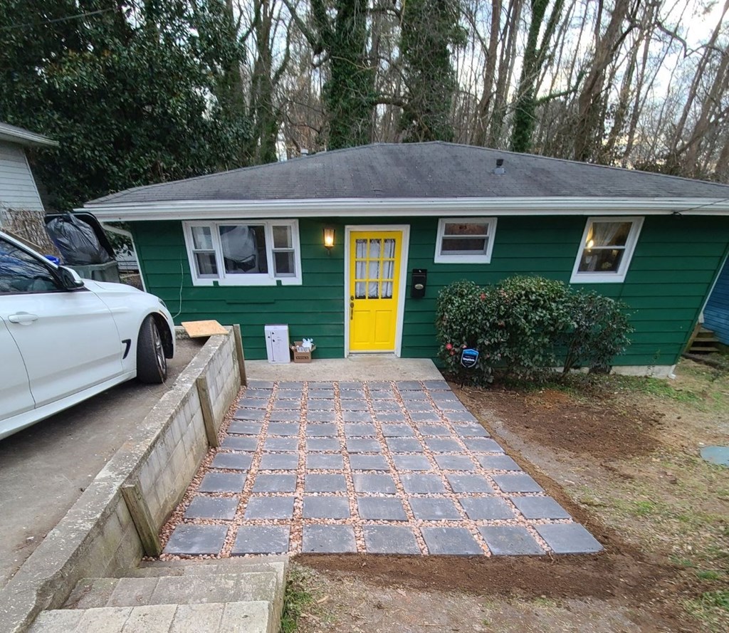 A green house with a yellow door and a white car parked in front.