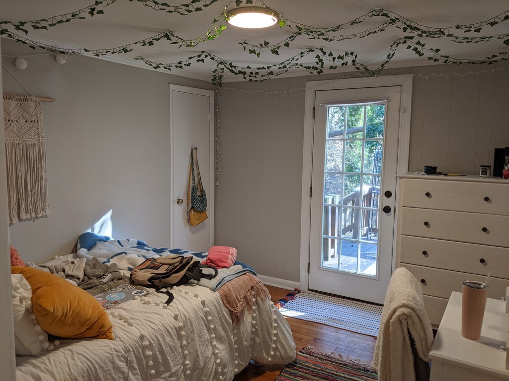 A messy bedroom with a bed in the center and a doorway leading to a balcony.