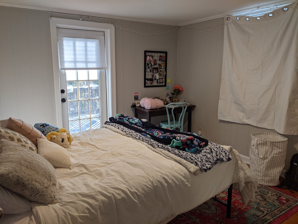 A bedroom with a bed covered in a white comforter and a window with blinds.