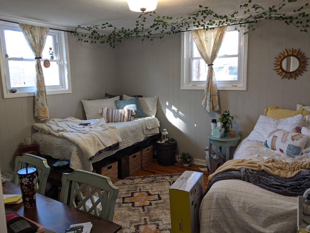 A bedroom with two beds, one with a yellow headboard, and a table with a vase on it.
