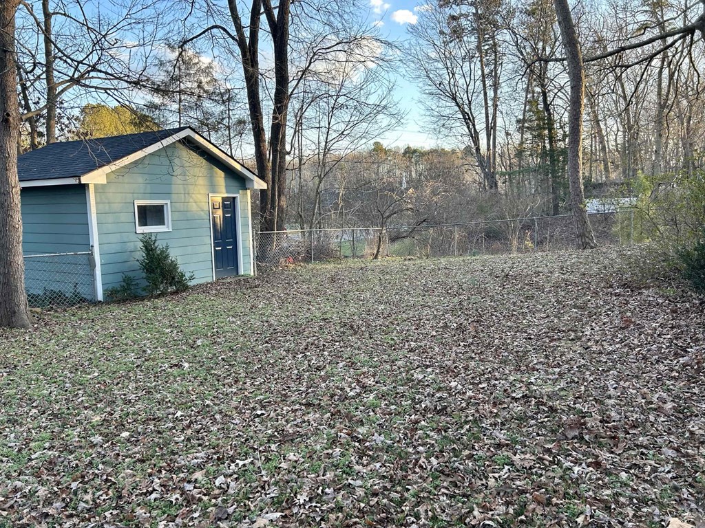 A small blue house with a black door is surrounded by trees and a field of fallen leaves.