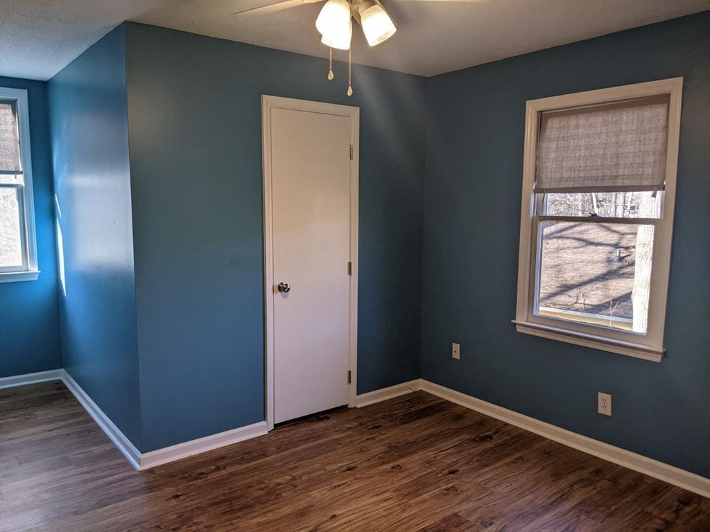 A room with a white door and a window with a view of a tree-lined street.