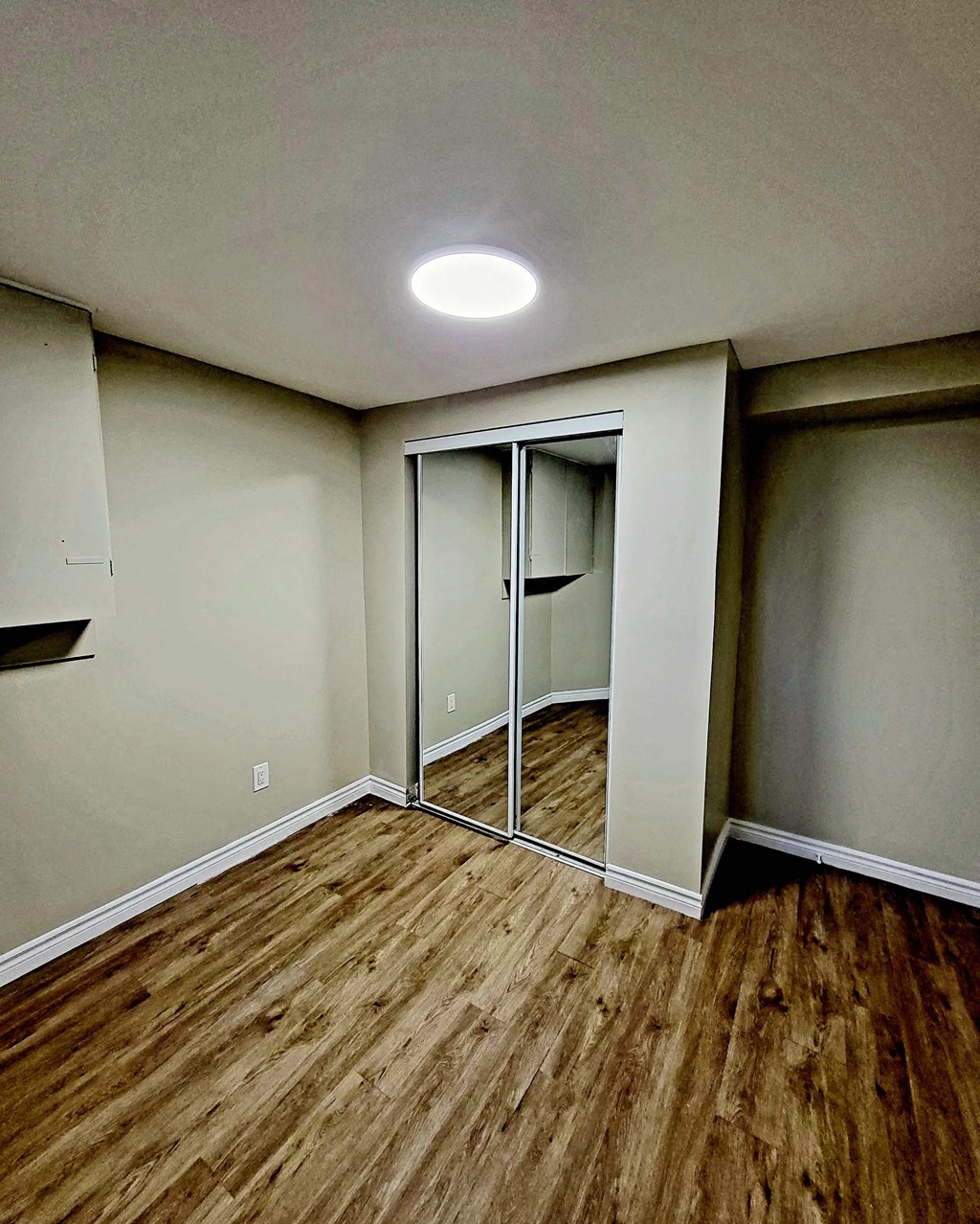 an empty room with wood flooring and mirrored closet doors