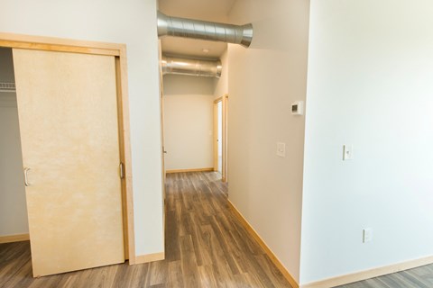 an empty room with a door and a hallway with wood floors and white walls