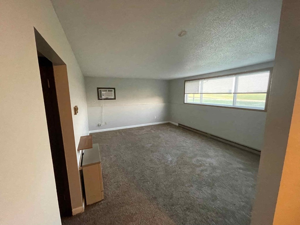 A room with a carpeted floor and a window with blinds.