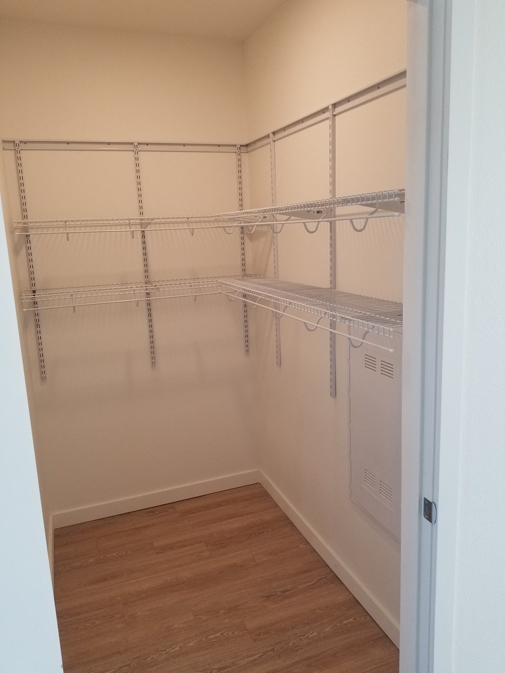 a walk in closet with white shelves and a wood floor