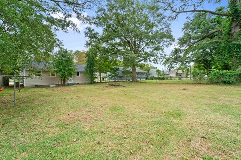 A backyard with a grassy area, trees, and a house in the background.