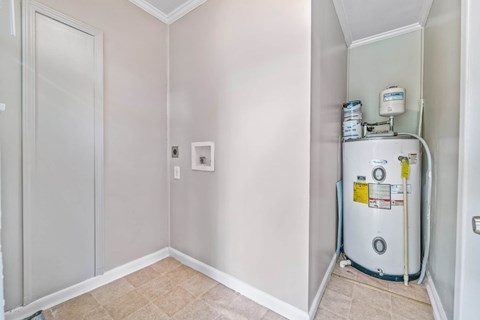A water heater is installed in a corner of a room with white walls and a white door.