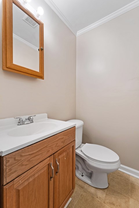 A white sink with a wooden cabinet and a white toilet in a bathroom.