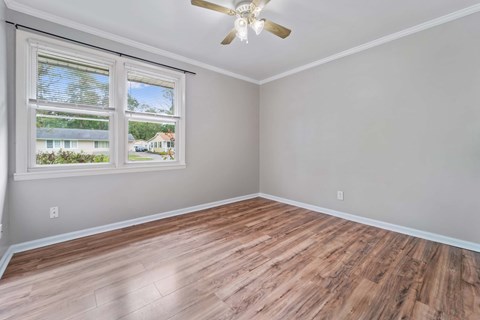 A room with a ceiling fan and a window overlooking a residential area.