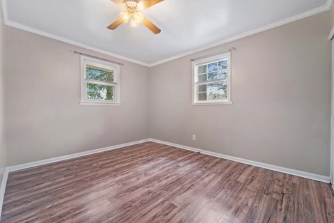 A room with a ceiling fan and two windows.