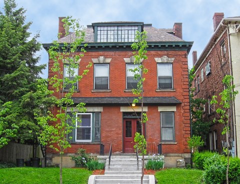 A red brick house with a green tree in front.
