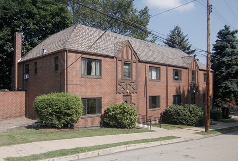 A red brick house with a black fence and green bushes in front.