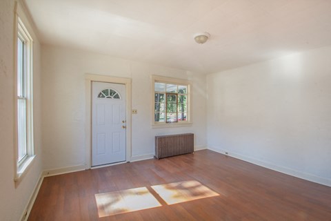 A room with a white door and a window with a view of trees outside.