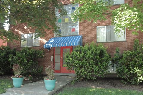 the front of a brick building with a red door and a blue awning
